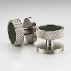 Pode incluir: Dois botões de armário prateados com acabamento texturizado. Um botão tem um centro verde e o outro tem um centro prateado.