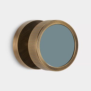 K&ouml;nnte beinhalten: Ein runder Spiegel in antikem Messing, mit einer grau-blauen reflektierenden Oberfl&auml;che. Der &auml;u&szlig;ere Ring hat eine geriffelte Textur, die R&uuml;ckseite ist flach. Minimalistisches und industrielles Design, passend f&uuml;r verschiedene Innenr&auml;ume.