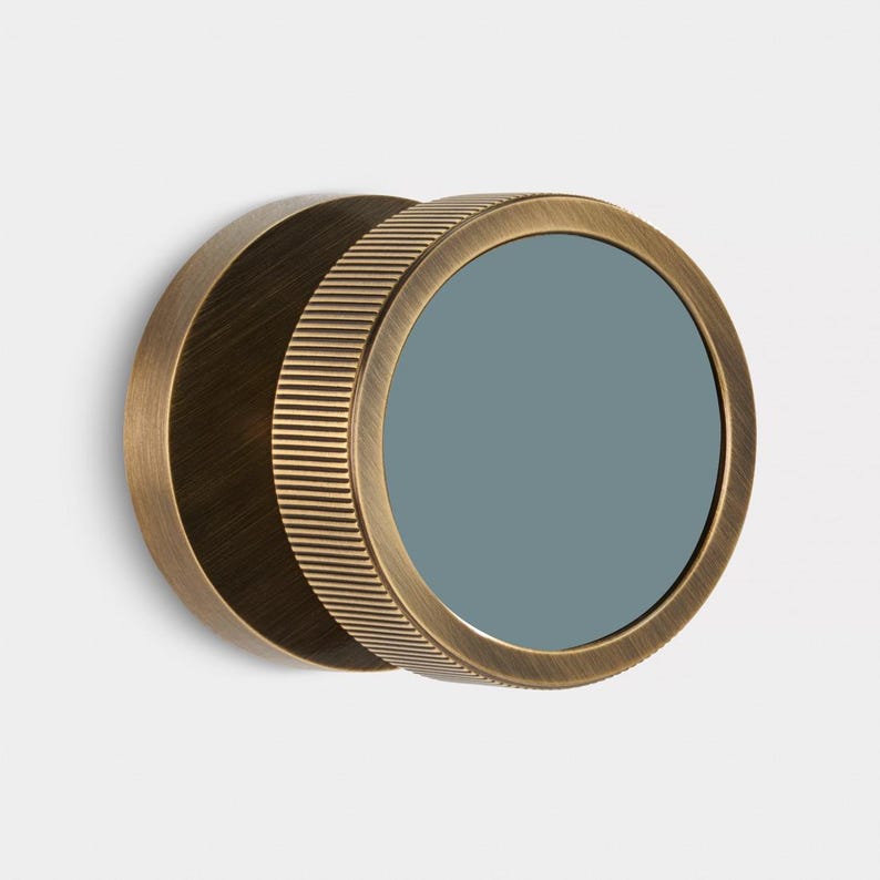 K&ouml;nnte beinhalten: Ein runder Spiegel in antikem Messing, mit einer grau-blauen reflektierenden Oberfl&auml;che. Der &auml;u&szlig;ere Ring hat eine geriffelte Textur, die R&uuml;ckseite ist flach. Minimalistisches und industrielles Design, passend f&uuml;r verschiedene Innenr&auml;ume.