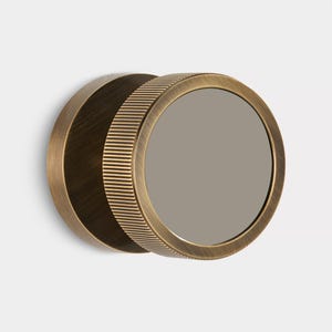 K&ouml;nnte beinhalten: Ein runder Wandspiegel in antik-messingfarbenem Finish. Der Spiegel hat einen geriffelten Au&szlig;enrand und eine dunkle, reflektierende Oberfl&auml;che. Das Design ist minimalistisch und industriell, mit einem Durchmesser von ca. 15 cm.