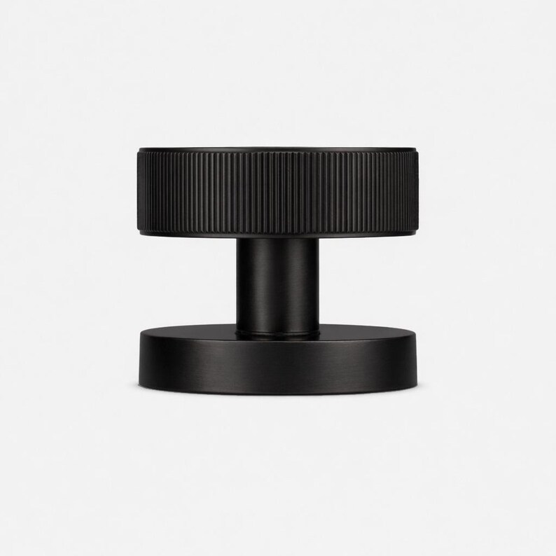 May include: A black, cylindrical door knob with a ridged top and a circular base. The knob has a minimalist design and is made of a matte black material. The door knob is suitable for interior doors.