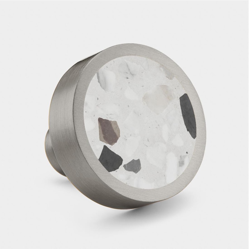 May include: A round, silver-toned cabinet knob with a white terrazzo inlay. The knob has a smooth, polished finish.