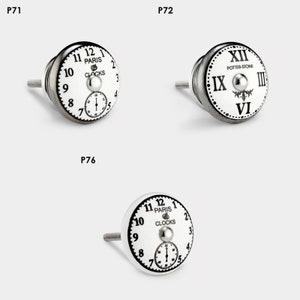 Puede incluir: Tres pomos de armario de cerámica blanca con un diseño de esfera de reloj. Los pomos tienen un tornillo de metal plateado y un pomo de metal plateado. El primer pomo tiene una esfera de reloj negra con números romanos y el texto "POTTER-STONE". El segundo y tercer pomo tienen una esfera de reloj negra con números arábigos y el texto "PARIS CLOCKS".