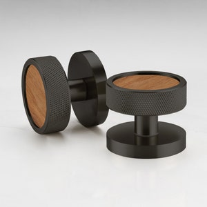 Puede incluir: Dos pomos de armario negros con un acento de madera. Los pomos tienen un diseño circular texturizado.