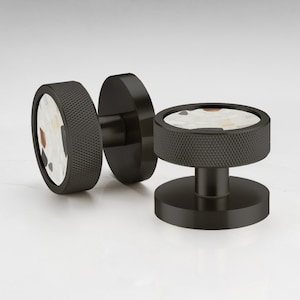 Pode incluir: Puxadores de armário em metal preto com uma pega texturizada e uma face circular. A face apresenta um fundo branco com manchas castanhas, pretas e vermelhas. Estes puxadores são projetados para móveis e decoração de casa.