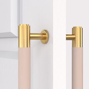 May include: A pair of gold door handles with a light pink leather grip. The handles are mounted on a white door.