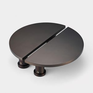 Peut inclure: Une poignée de porte en forme de cercle divisé en bronze foncé. La poignée est composée de deux demi-cercles reliés par une fine bande de métal. La poignée est fixée au mur à l'aide de deux vis.