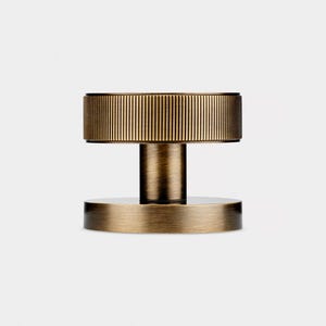 K&ouml;nnte beinhalten: Ein bronzefarbener T&uuml;rknauf mit geriffelter, zylindrischer Oberseite und kreisf&ouml;rmiger Basis. Der Knauf ist durch einen kurzen, zylindrischen Schaft verbunden. Das Design ist minimalistisch und modern, passend f&uuml;r verschiedene Einrichtungsstile. Ma&szlig;e in Zentimetern.