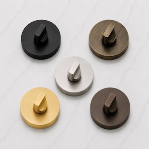 May include: Five circular wall hooks arranged in a pentagonal pattern. Each hook features a flat, round base and a central, curved knob. The finishes include matte black, brushed brass, brushed silver, antique bronze, and dark brown metal.