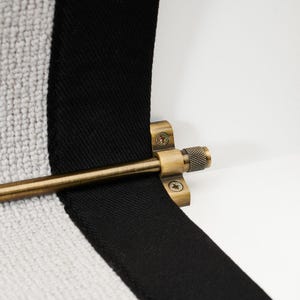 May include: Close-up of a brass towel bar with a textured knob, mounted on a white wall. A black and white striped towel is draped over the bar, creating a modern, minimalist aesthetic.