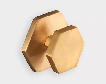 May include: A brushed brass cabinet knob featuring a hexagonal face and a matching hexagonal backplate. The metal has a warm, golden-toned finish with a subtle, linear texture across the flat surfaces of the geometric hardware piece.
