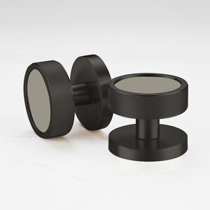 Może przedstawiać: Trzy czarne obiekty w kształcie hantli o okrągłym kształcie. Obiekty mają matowe wykończenie i żebrowaną fakturę po bokach. Środek każdego obiektu jest jasnoszary.