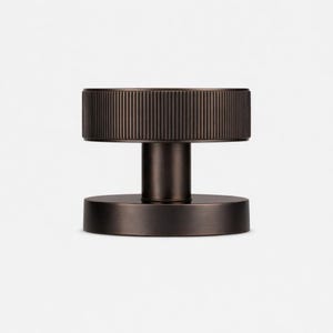 Puede incluir: Un pomo de puerta de color bronce con una parte superior cil&iacute;ndrica estriada y una base circular. El pomo tiene un v&aacute;stago cil&iacute;ndrico corto. Dise&ntilde;o minimalista y moderno.