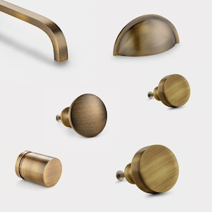 May include: Assortment of antique brass cabinet hardware, including a pull handle, a cup pull, and three knobs.