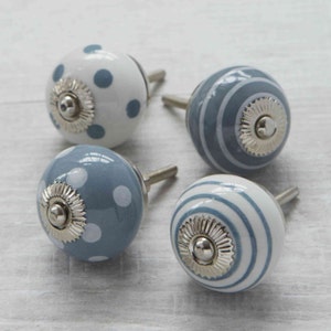 May include: Four decorative ceramic cabinet knobs. Two knobs are white with blue polka dots, and two are blue with white polka dots. The other two knobs are white with blue stripes and blue with white stripes. Each knob has a silver metal base and stem.