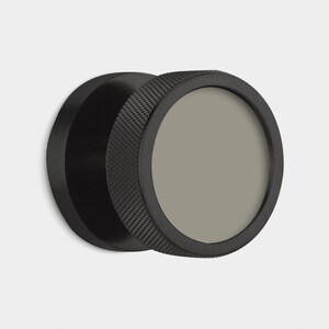 May include: A black, circular object with a textured outer ring and a smooth, gray center. The object appears to be made of metal and has a modern, minimalist design. The textured ring adds a tactile element to the design.