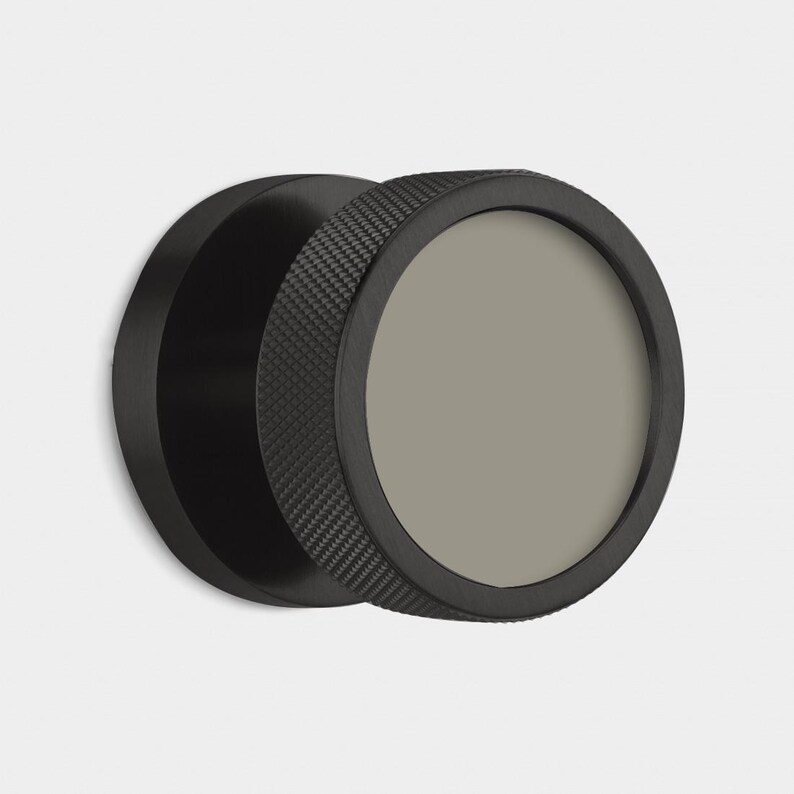 May include: A black, circular object with a textured outer ring and a smooth, gray center. The object appears to be made of metal and has a modern, minimalist design. The textured ring adds a tactile element to the design.