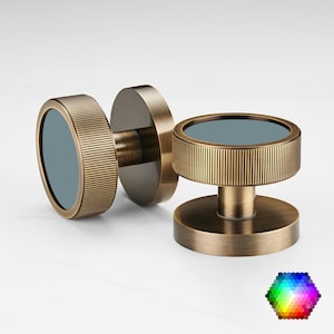 May include: Two antique brass cabinet knobs with a circular design. Each knob has a ridged, cylindrical outer ring and a flat, circular centre with a muted blue-grey finish. The knobs are displayed on a white surface.