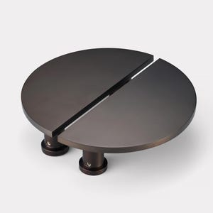 May include: A dark bronze-colored, semi-circular table with a split top design. The table is supported by two cylindrical legs. The table's dimensions are approximately 24 inches in diameter and 12 inches in height.