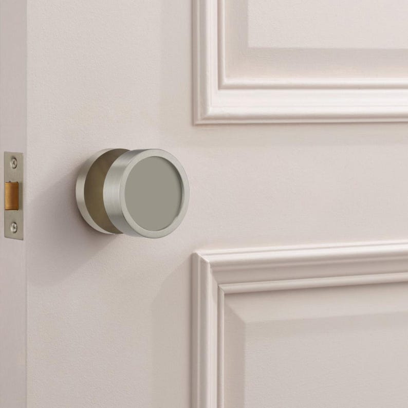 Puede incluir: Pomo de puerta moderno de n&iacute;quel cepillado. El dise&ntilde;o circular est&aacute; montado en una puerta blanca, con un marco de puerta a juego. La puerta tambi&eacute;n tiene un pestillo plateado.