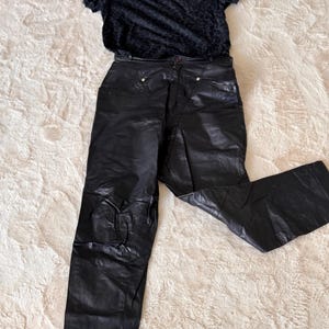 Könnte beinhalten: Ein schwarzes kurzärmeliges T-Shirt mit dezentem Ton-in-Ton-Leopardenmuster, kombiniert mit einer schwarzen Hose mit hoher Taille, glatter Oberfläche, Knopfverschluss am Bund und sichtbaren Nahtdetails im vorderen Hüftbereich.
