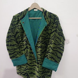 May include: A long-sleeved jacket featuring a green and black tiger-stripe pattern on the exterior. The interior lining and the folded cuffs display a contrasting vertical stripe pattern in shades of blue and green. A single button is visible.