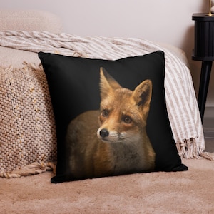 May include: A square throw cushion featuring a high-resolution photographic print of a red fox against a solid black background. The fox is shown from the chest up, displaying its orange and white fur, pointed ears, and dark eyes.