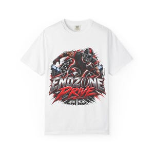 May include: A white short-sleeve t-shirt featuring a graphic of a football player in a black and red uniform running with a ball. The text ENDZONE DRIVE is printed in large metallic letters above the number 50, with stadium lights and play diagrams.