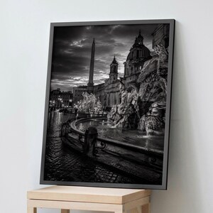 Puede incluir: Una impresión de arte mural enmarcada en blanco y negro que representa la Piazza Navona en Roma al atardecer. La escena muestra la Fuente de los Cuatro Ríos con su obelisco central, esculturas de piedra ornamentadas y un estanque bajo un cielo nublado.