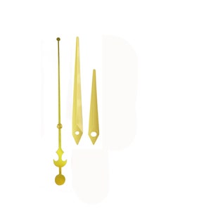 May include: A set of four gold-colored clock hands. The set includes a long, thin second hand, two hour and minute hands with pointed ends, and a decorative counterweight. The hands are designed for a clock.