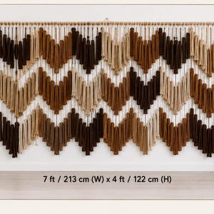 May include: A large macrame wall hanging featuring a chevron pattern in shades of cream, tan, and dark brown. The piece is suspended from a wooden rod and measures 213 cm (W) x 122 cm (H). The text 'VARIATION 1' is visible in the top left corner.