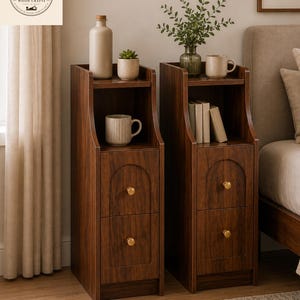May include: Two tall, narrow dark wood nightstands featuring an open top shelf and two lower drawers with arched detailing and small gold-toned knobs. The nightstands are positioned side-by-side, each displaying items like a bottle, mug, and books.