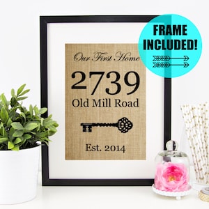 May include: A black framed print with a burlap background. The print says "Our First Home" with the address "2739 Old Mill Road" and the date "Est. 2014". A black key is pictured below the address.