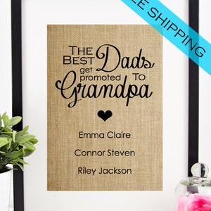 May include: Framed print with the text "THE BEST Dads get promoted to Grandpa" in black script on a burlap background. Below the text are three names: Emma Claire, Connor Steven, and Riley Jackson. The frame is black.