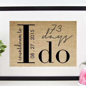 May include: A framed burlap print with the text "countdown to I do" and the date "08.27.2015". The print also includes the text "73 days" written in cursive.