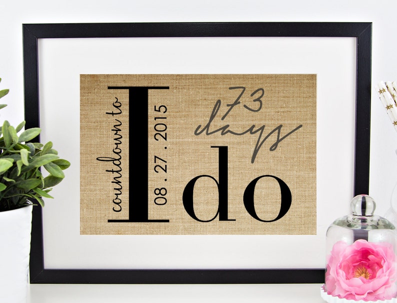 May include: A framed burlap print with the text "countdown to I do" and the date "08.27.2015". The print also includes the text "73 days" written in cursive.