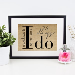 May include: A framed burlap print with the text "countdown to I do" and the date "08.27.2015". The print also includes the text "73 days" written in cursive.