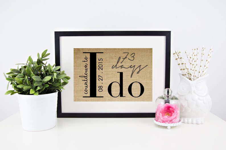 May include: A framed burlap print with the text "countdown to I do" and the date "08.27.2015". The print also includes the text "73 days" written in cursive.