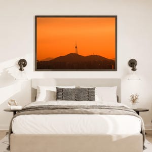 Puede incluir: Un dormitorio con una cama de ropa blanca y un coj&iacute;n con patr&oacute;n de chevr&oacute;n en blanco y negro, flanqueado por dos peque&ntilde;as mesas auxiliares redondas con l&aacute;mparas de pared. Sobre la cama cuelga un cuadro de un horizonte urbano al atardecer.