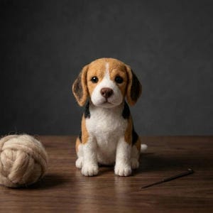 May include: A needle-felted beagle puppy figurine with brown, black, and white fur, dark eyes, and a brown nose. Beside the puppy sits a ball of light tan wool yarn and a single metal sewing needle, showcasing the craft of needle felting.