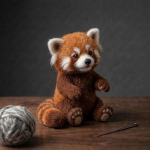 May include: A needle-felted red panda figurine with a textured, fuzzy brown and orange coat, white facial markings, and small paws with visible pads. The figure is seated upright, featuring a round tail and dark, expressive eyes.