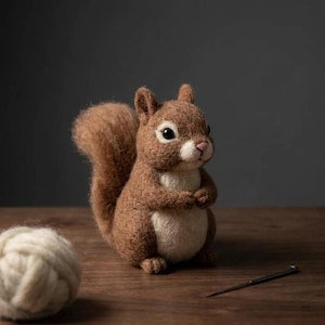 May include: A needle-felted squirrel figurine crafted from brown and cream wool. The squirrel has a bushy tail, dark eyes, a small pink nose, and a white chest. Beside the squirrel sits a ball of cream yarn and a single metal sewing needle.
