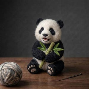 Könnte beinhalten: Eine nadelgefilzte Panda-Figur aus schwarzer und weißer Wolle, die einen kleinen grünen Bambuszweig aus Filz in den Pfoten hält. Der Panda hat eine strukturierte Oberfläche, dunkle Augen und helle Pfotenballen an den Füßen.