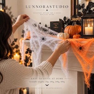 Op de afbeelding: Wit en oranje decoratief spinnenwebmateriaal met zwarte plastic spinnen. Het product is verkrijgbaar in gewichten van 20g, 100g, 240g en 500g. De tekst LUNNORASTUDIO, SEASONAL DECOR FOR A MORE MAGICAL HOME en EASY TO STYLE AT HOME is zichtbaar.