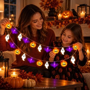 May include: A string of Halloween LED lights featuring alternating orange jack-o'-lanterns, white ghosts, and purple bats. The decorative light strand is held by two individuals and includes multiple illuminated figures along a thin wire cable.