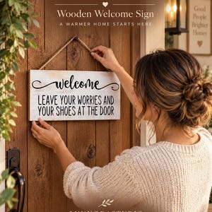 Puede incluir: Un letrero rectangular de madera con un acabado blanco desgastado y texto negro que dice welcome LEAVE YOUR WORRIES AND YOUR SHOES AT THE DOOR. El letrero cuenta con una cuerda de yute para colgar en la parte superior y está en una puerta.