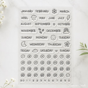 Puede incluir: Un juego de sellos de fotopolímero transparente con contornos de tinta negra de los meses del año, días de la semana, números del uno al treinta y uno, y varios iconos que incluyen un copo de nieve, nube, rayo, estrella, sol, luna y flor.