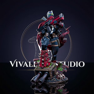 May include: A detailed collectible figurine of a masked character in a dark suit with a red cape, holding a large red and black rifle. The figure stands on a base featuring a heavy weapon, skulls, and debris, with the text VIVALE STUDIO visible.
