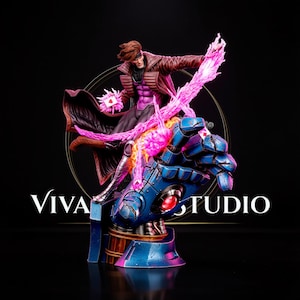 May include: A collectible figurine of a character with brown hair wearing a brown trench coat and purple shirt, standing on a large blue robotic hand. The character holds a glowing pink energy effect and playing cards. The text Viva Studio is visible.