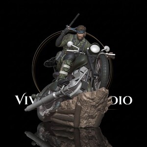Pode incluir: Uma figura colecionável detalhada de um soldado em traje de camuflagem verde montado numa motocicleta preta. A figura usa uma bandana azul e segura um cassetete. A moto está posicionada sobre uma base de rocha castanha com o texto VIV STUDIO.